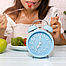 Nahaufnahme der blauen Uhr, die junge Frau beim Zuhause-Gesunden-Lifestyle-Konzept mit Früchten frisst und auf einem Tisch sitzt.