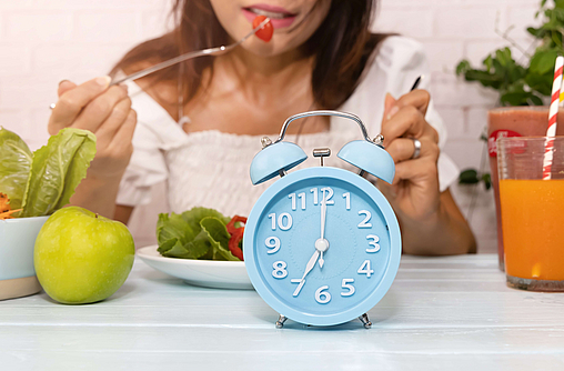 Nahaufnahme der blauen Uhr, die junge Frau beim Zuhause-Gesunden-Lifestyle-Konzept mit Früchten frisst und auf einem Tisch sitzt.
