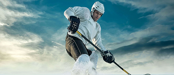 Ein Eishockeyspieler auf dem Eis. Er bremst scharf vor dem Puk. Das Eis spritzt.
