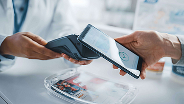 Ein Kunde steht in einer Apotheke. Er löst per Smartphone ein e-Rezept ein.