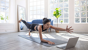 Junge Frau nimmt daheim in einem großen Raum an einem Online-Kurs teil.