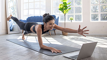 Junge Frau nimmt daheim in einem großen Raum an einem Online-Kurs teil. 