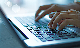 Nahaufnahme von zwei Händen, die etwas auf der Tastatur eines Laptops eintippen.