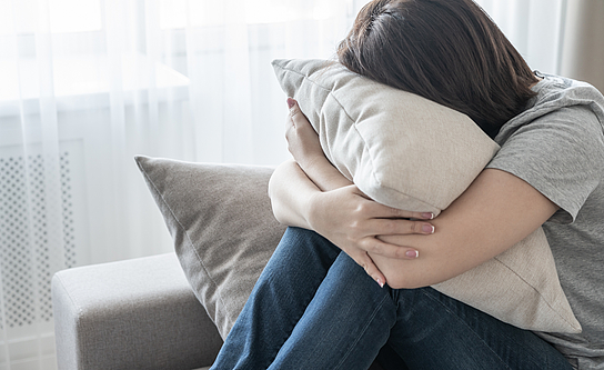 Frau sitzt auf dem Sofa und hat ihr Gesicht in ein Kissen gedrückt.