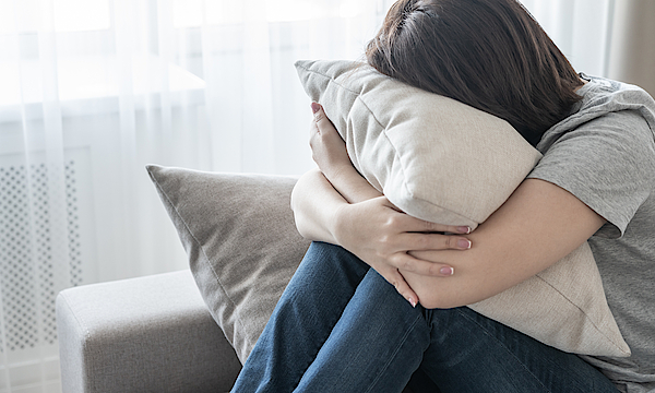 Frau sitzt auf dem Sofa und hat ihr Gesicht in ein Kissen gedrückt.