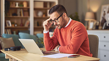 Ein Mann sitzt in der Küche und liest etwas in seinem Laptop.