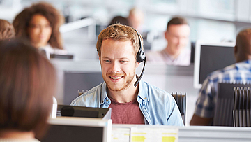 In einem Callcenter sitzt ein junger Mann mit Headset und telefoniert.
