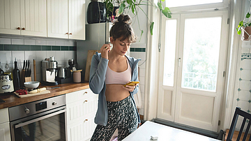 Frau steht in der Küche und steckt einen Ohrhörer des Smartphones in ein Ohr.