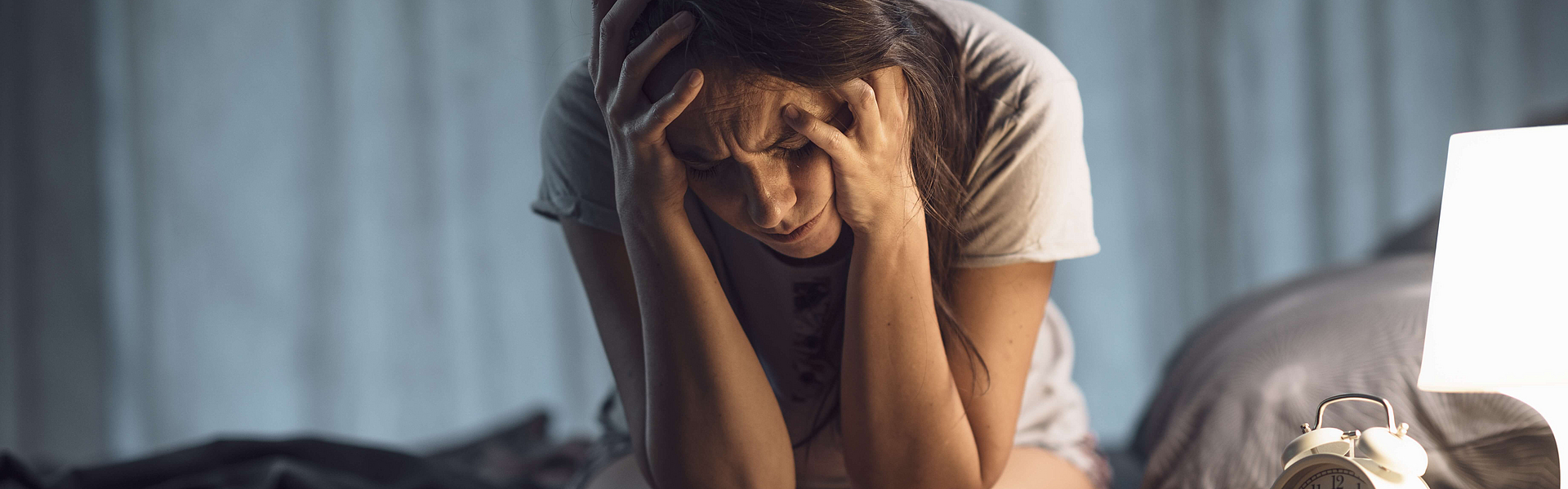 Schlechter Schlaf hat Folgen für die Gesundheit. Frau sitzt nachts verzweifelt auf ihrem Bett, sie kann nicht schlafen.