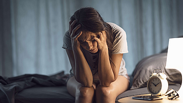 Frau sitzt nachts verzweifelt auf ihrem Bett, sie kann nicht schlafen.