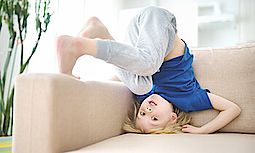 Ein kleiner Junge turnt auf einem hellen Sofa herum.