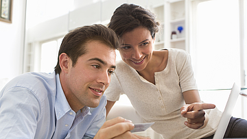 Ein Paar sitzt vor einem Laptop und besprechen den Inhalt der aufgerufenen Website.