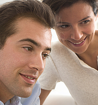 Ein Paar sitzt vor einem Laptop und besprechen den Inhalt der aufgerufenen Website.