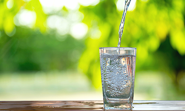 Auf einem Tisch steht ein Glas Wasser. Es wird eingeschenkt.