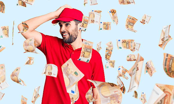 Ein junger Mann in der Uniform eines Lieferantenmit Baseball-Kappe freut sich über Geldsegen. Die Scheine fliegen um ihn herum.