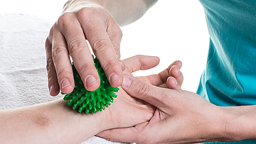 Therapeut behandelt den Arm eines Patienten mit einem Igelball.