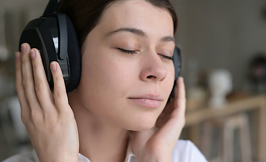 Frau mit Kopfhörern hört mit geschlossenen Augen Musik.