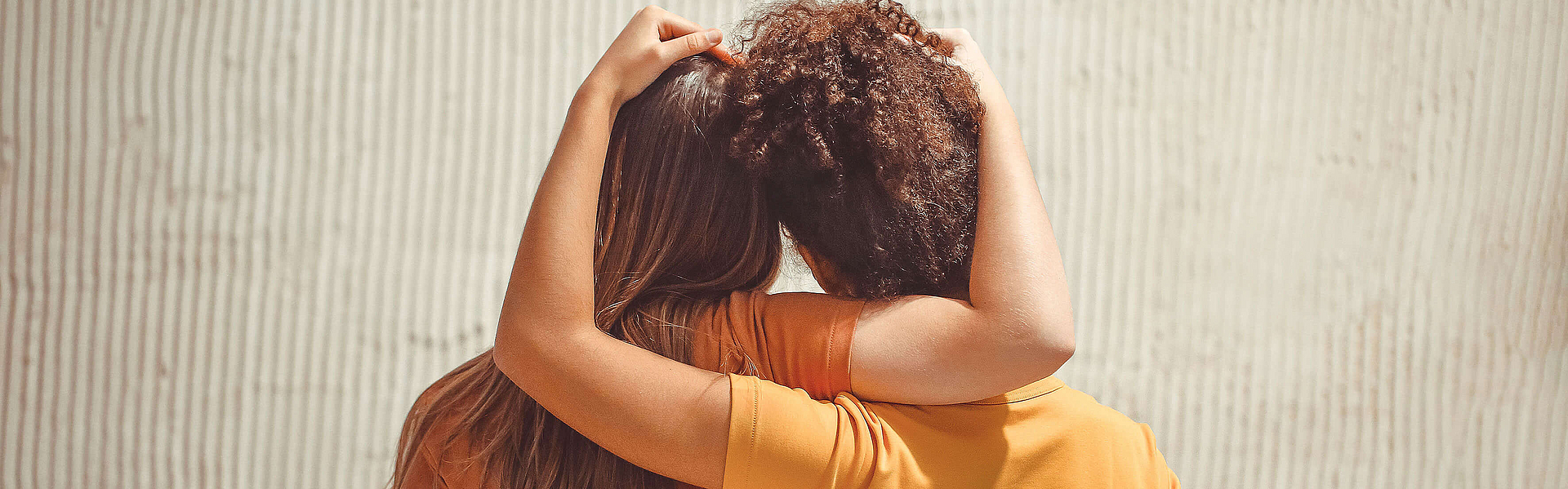 Rückansicht von zwei Mädchen die sich an den Händen halten und umarmen.