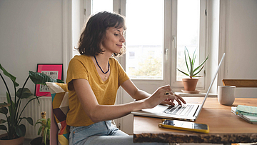 Frau ist im Homeoffice, sie sitzt mit geöffnetem Laptop am Esszimmertisch.