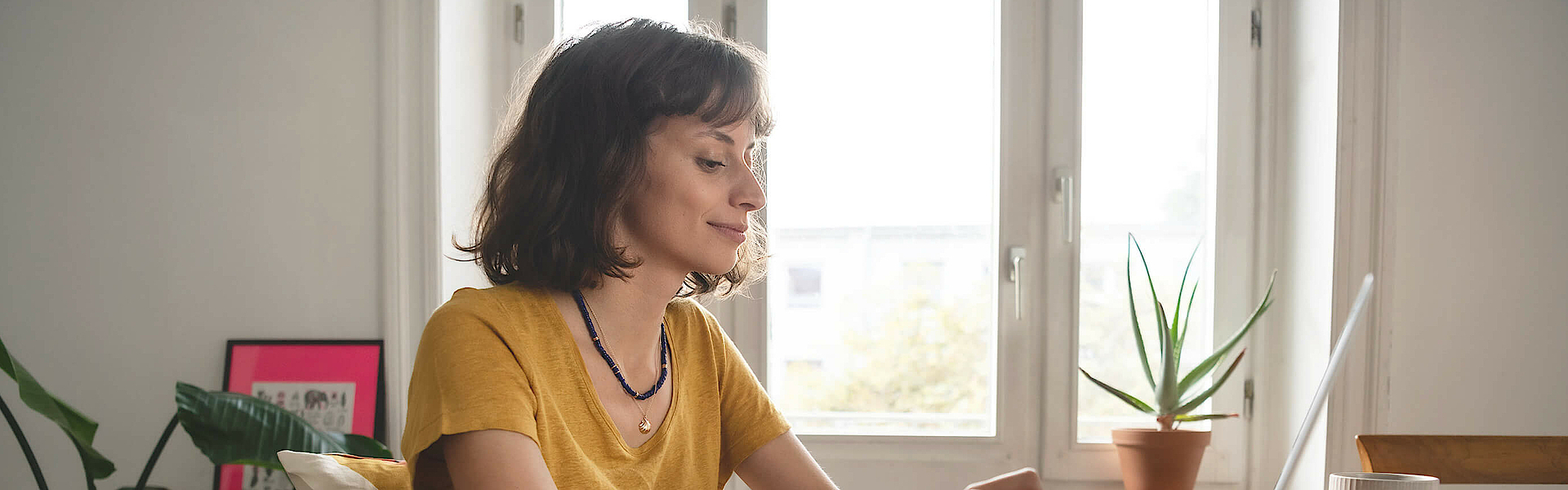 Frau ist im Homeoffice, sie sitzt am Esszimmertisch. Der geöffnete Laptop steht vor ihr.