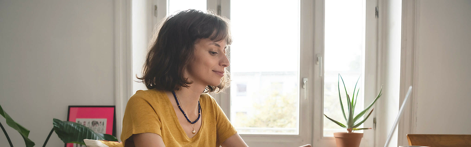 Frau ist im Homeoffice, sie sitzt am Esszimmertisch. Der geöffnete Laptop steht vor ihr.