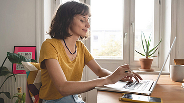 Frau ist im Homeoffice, sie sitzt mit geöffnetem Laptop am Esszimmertisch.