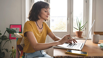 Frau ist im Homeoffice, sie sitzt mit geöffnetem Laptop am Esszimmertisch.