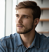 Ein Mann sitzt am Schreibtisch und schaut nachdenklich aus dem Fenster.