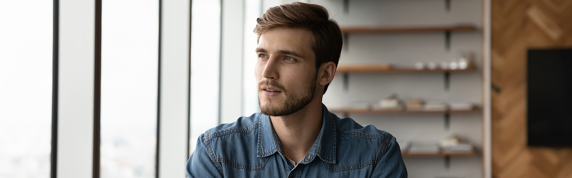 Ein Mann sitzt am Schreibtisch und schaut nachdenklich aus dem Fenster.