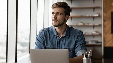 Ein Mann sitzt am Schreibtisch und schaut nachdenklich aus dem Fenster.