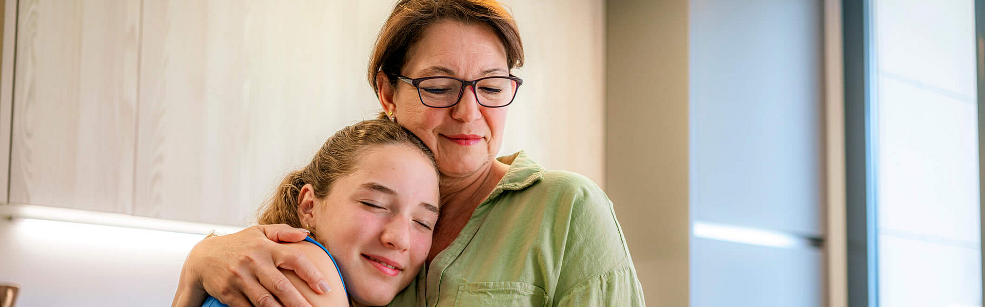 Familienbasierte Therapie bei Jugendlichen mit Essstörung Mutter umarmt jugendliche Tochter am Frühstückstisch