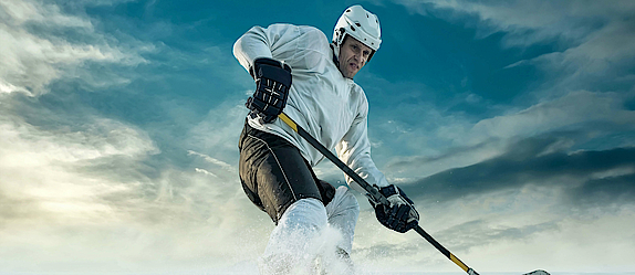 Ein Eishockeyspieler auf dem Eis. Er bremst scharf vor dem Puk. Das Eis spritzt.