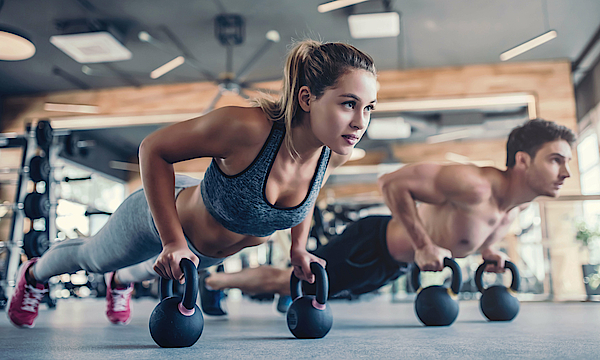 Ein Mann und eine Frau trainiere in einem Fitnessstudio mit Gewichten. Sie machen Liegestütz mit diesen Gewichten.