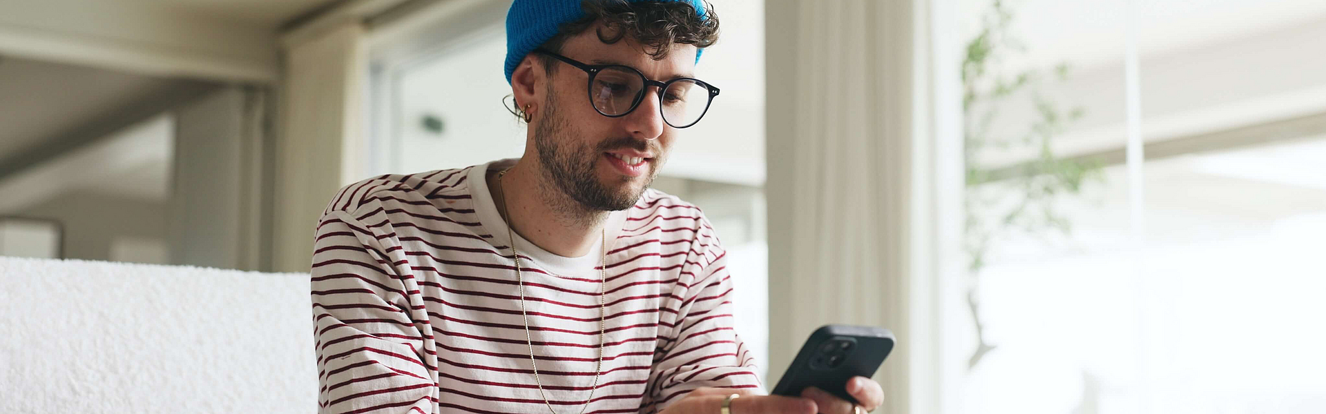 Junger Mann benützt das Smartphone er sitzt auf der Couch.