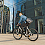 Ein lächelnder junger Mann fährt mit dem Fahrrad an einem modernen Glasgebäude vorbei.