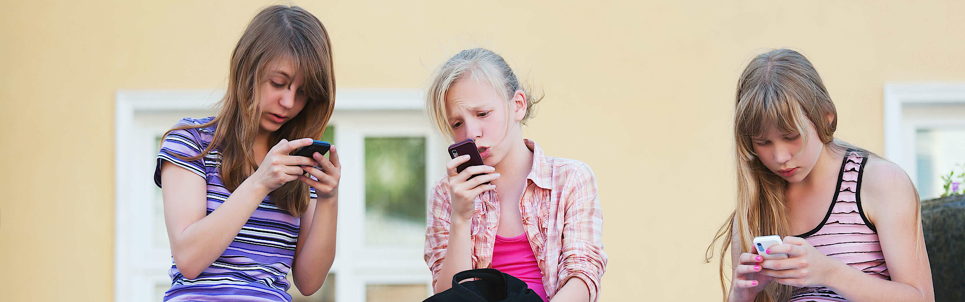 Drei Mädchen sitzen auf einer Balustrade aus Stein. Sie alle schauen in ihr Handy.