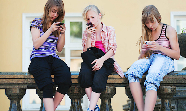 Drei Mädchen sitzen auf einer Balustrade aus Stein. Sie alle schauen in ihr Handy.