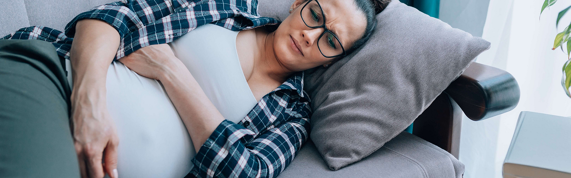 Junge traurige schwangere Frau liegt auf einem Sofa. Sie hat möglicherweise eine Schwangerschaftsdepression.