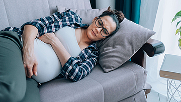 Schwangere traurige Frau liegt auf dem Sofa. Sie hat vielleicht eine Schwangerschaftsdepression.