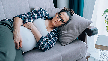 Schwangere traurige Frau liegt auf dem Sofa. Sie hat vielleicht eine Schwangerschaftsdepression.