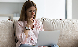 Eine Frau sitz auf einem Sofa und schaut auf ihren Laptop
