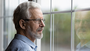 Ein älterer Mann schaut nachdenklich aus dem Fenster er war bei der Darmkrebsvorsorge.