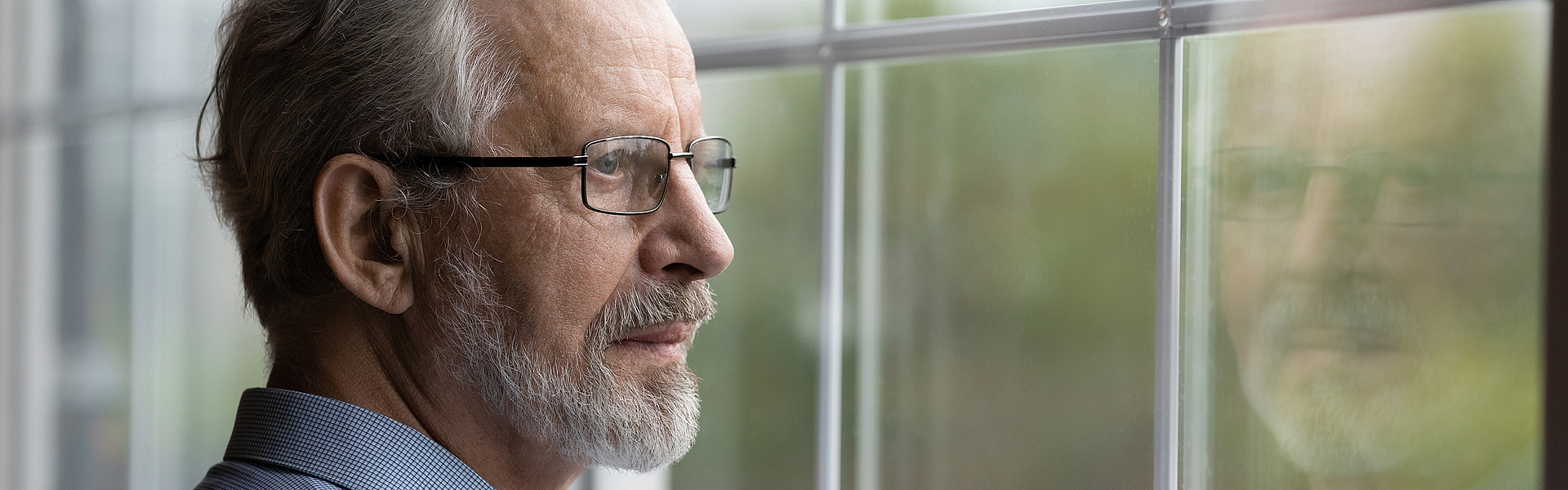Ein älterer Mann schaut nachdenklich aus dem Fenster er war bei der Darmkrebsvorsorge.