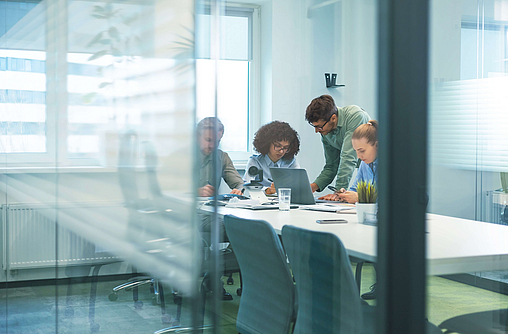 Zwei Frauen und ein Mann sind in einem Geschäftsbüro hinter Glasscheiben.