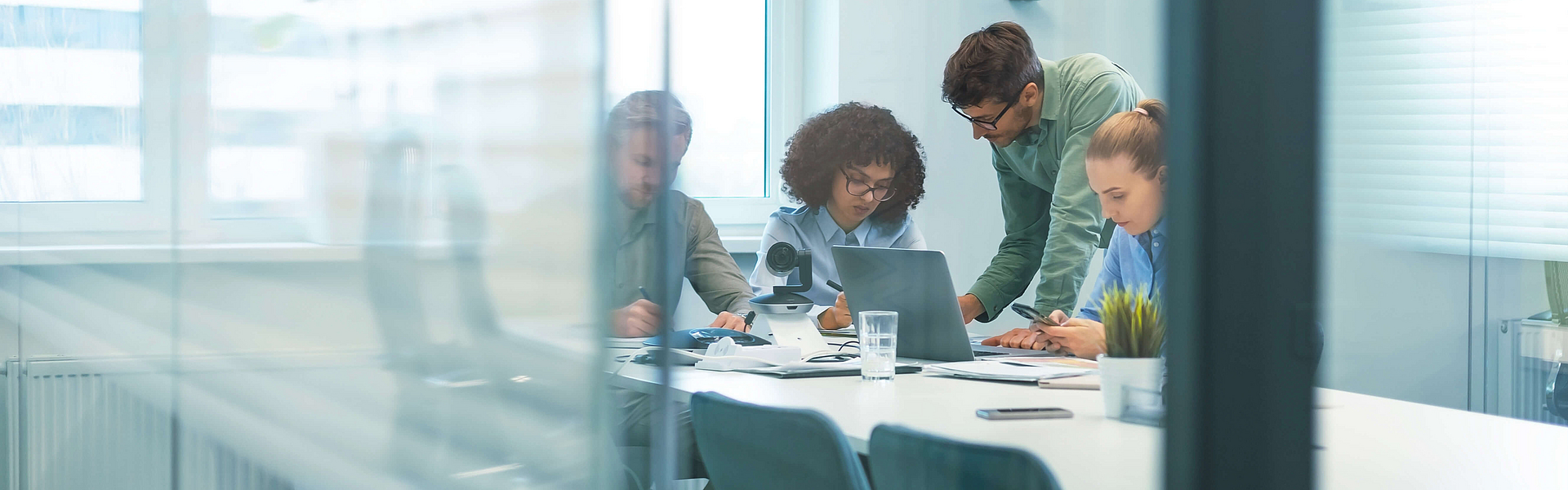 Zwei Frauen und ein Mann sind in einem Geschäftsbüro hinter Glasscheiben.