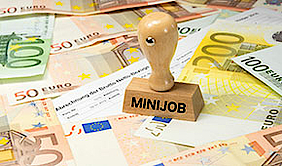 Lohnabrechnung, größtenteils verdeckt von Geldscheinen. Darauf steht ein Stempel aus Holz mit der Aufschrift "Minijob".