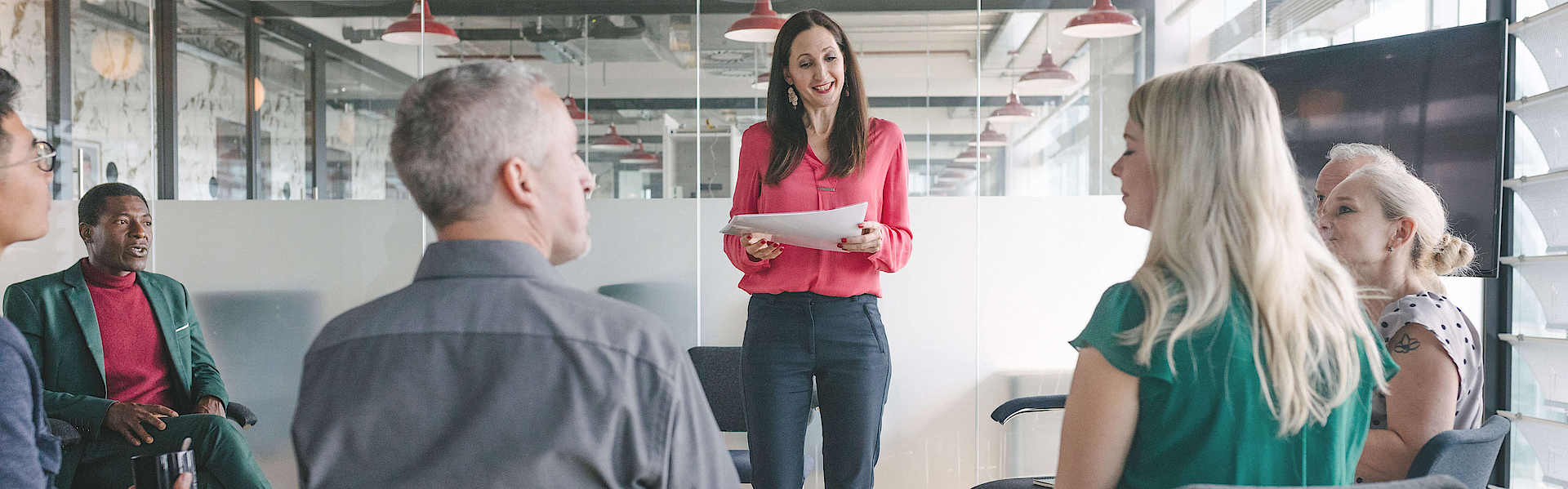 Im Büro, eine Frau hält ihren sitzenden Kollegen im Stehen einen Vortrag.