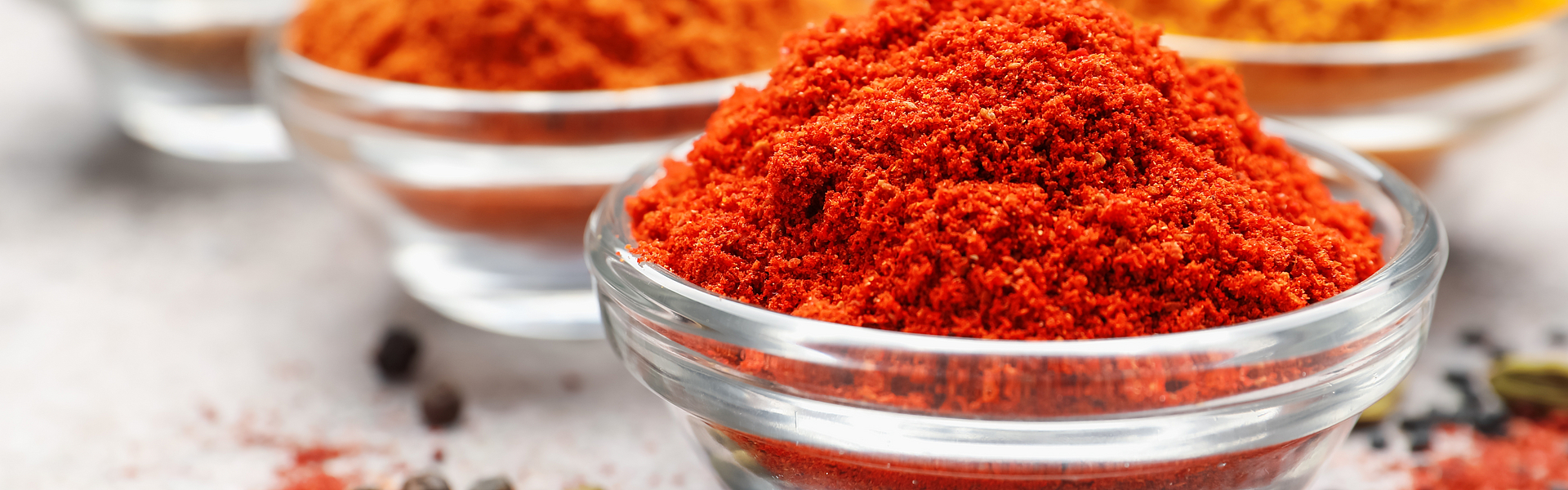 drei Glasschälchen mit scharfen Gewürzen wie Chili, Curry oder Paprika stehen auf einer Oberfläche