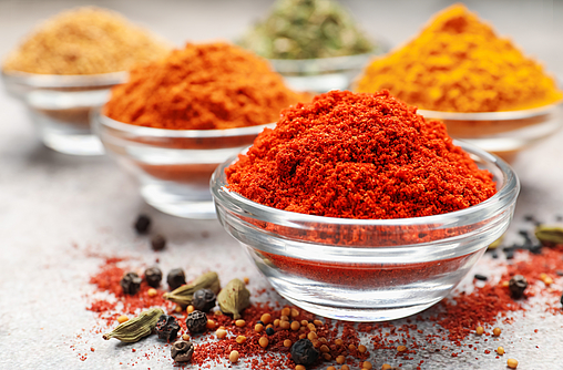 drei Glasschälchen mit scharfen Gewürzen wie Chili, Curry oder Paprika stehen auf einer Oberfläche