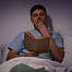 Junger müder Mann sitzt im Halbdunkeln im Bett und liest.